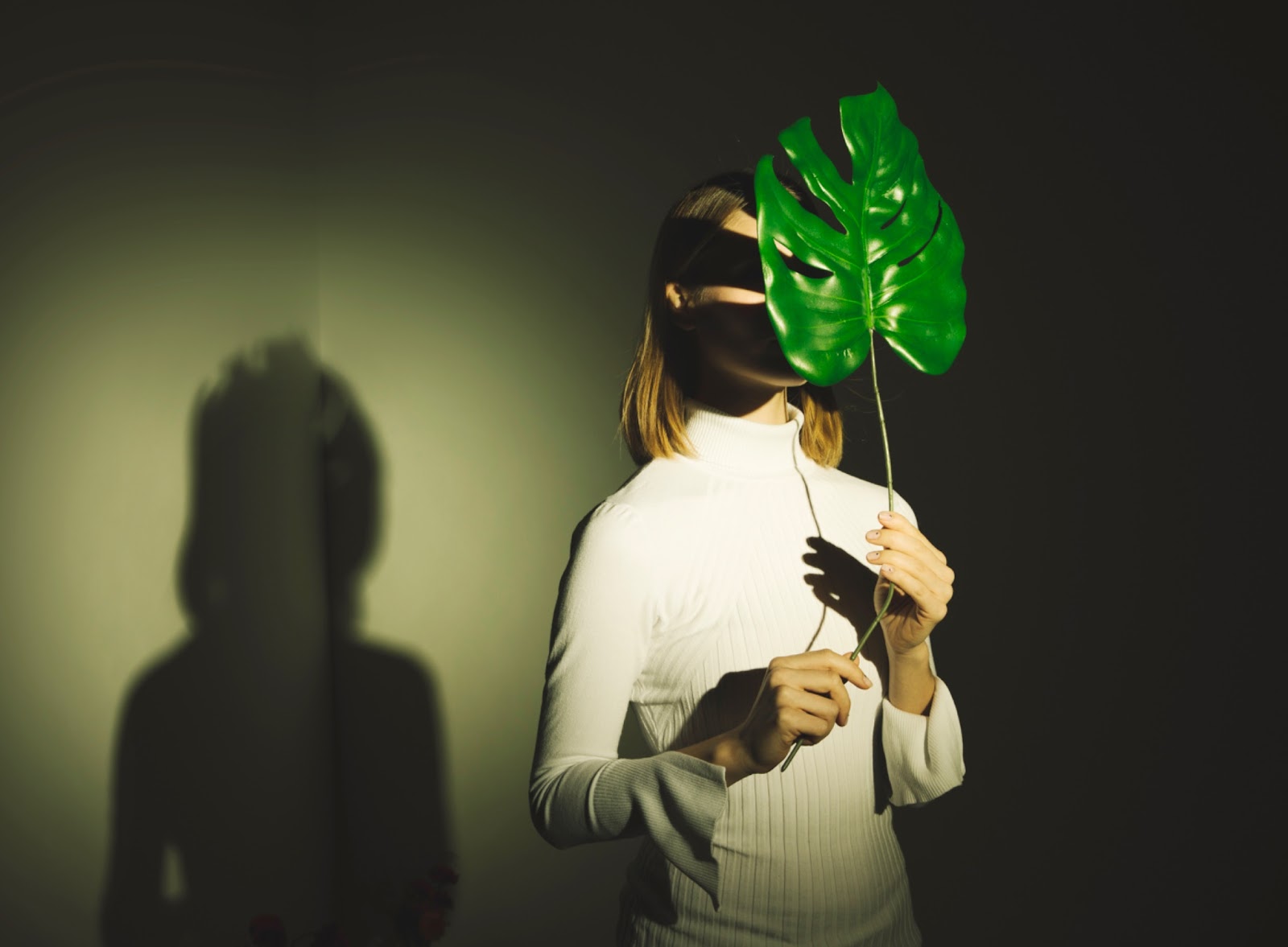 A woman covering her face with a big green leaf