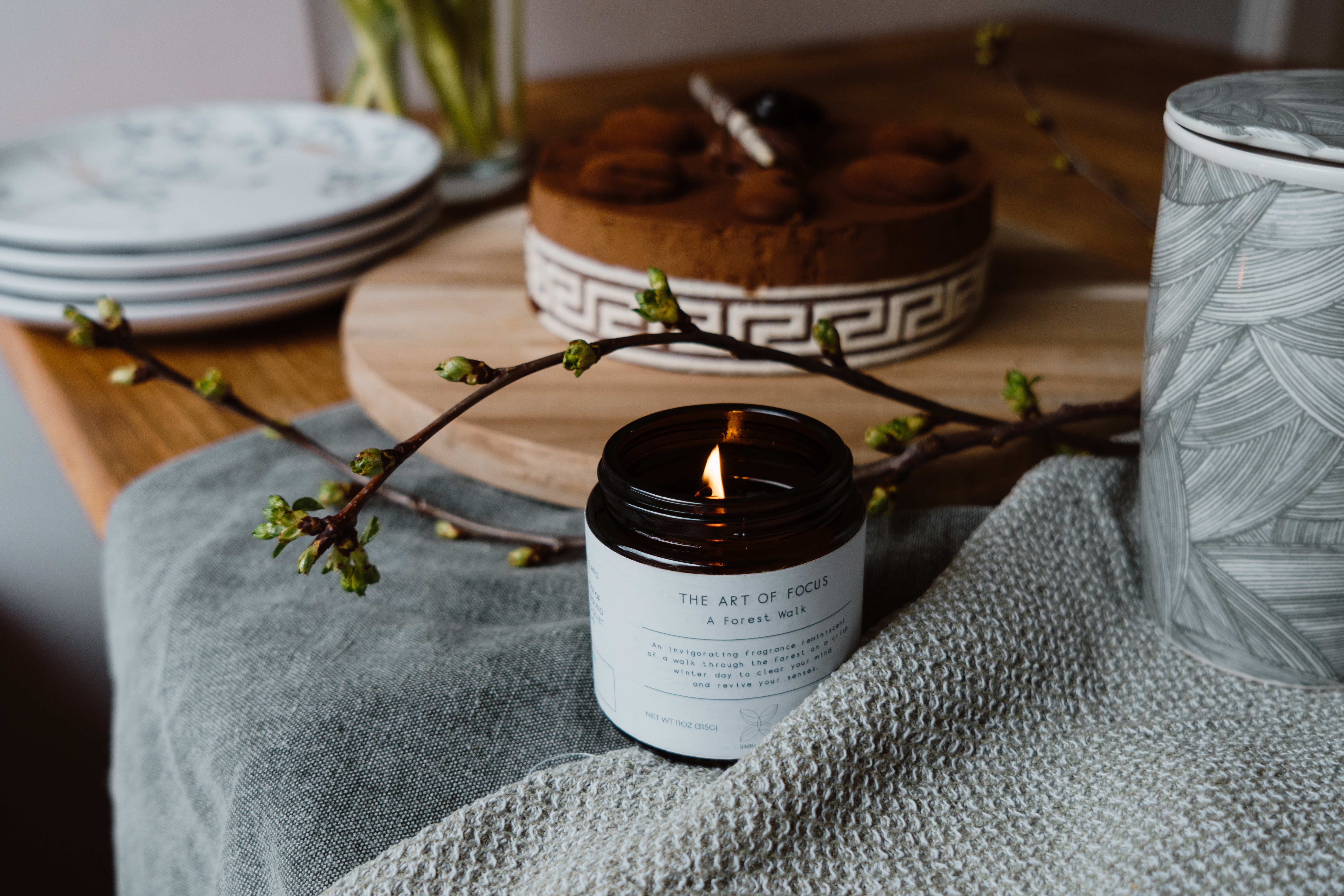 A lighting candle with a chocolate cake and a vase in the background